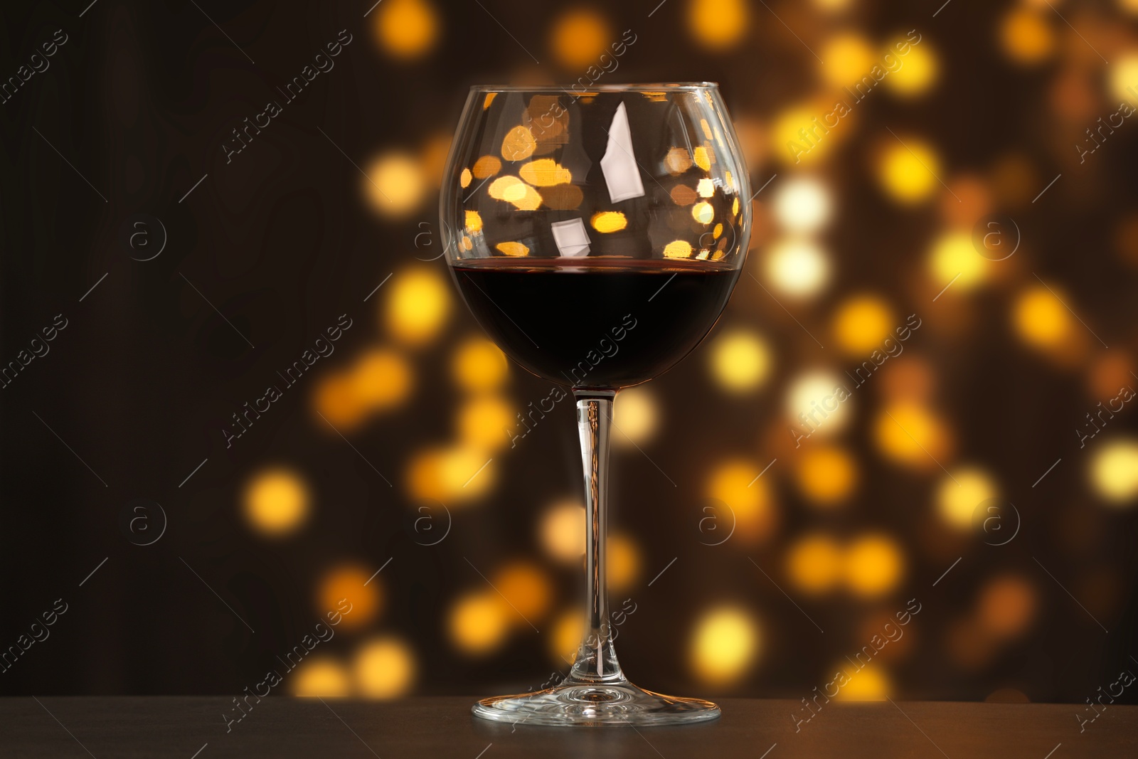 Photo of Tasty red wine in glass on table against dark background with blurred lights, bokeh effect