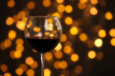 Photo of Tasty red wine in glass against dark background with blurred lights, closeup. Bokeh effect