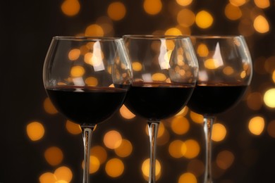 Photo of Tasty red wine in glasses against dark background with blurred lights, closeup. Bokeh effect