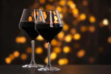 Photo of Tasty red wine in glasses on table against dark background with blurred lights, bokeh effect. Space for text