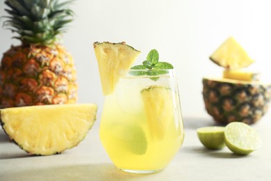 Photo of Tasty pineapple cocktail with mint in glass on light table