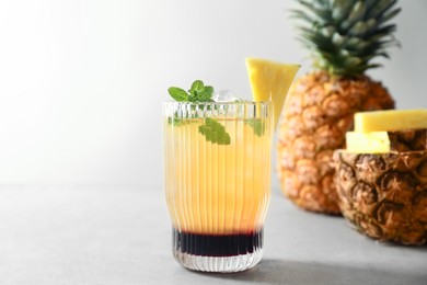 Photo of Tasty pineapple cocktail with mint in glass served on light table