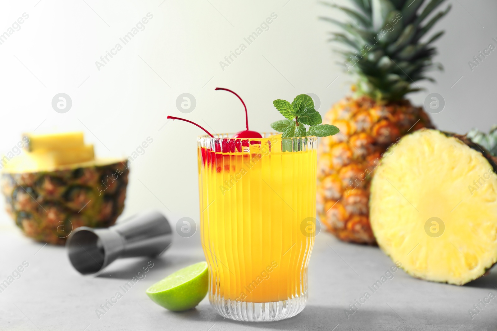 Photo of Tasty pineapple cocktail with mint and cherry in glass served on light table