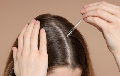 Photo of Hair loss problem. Girl applying serum onto hairline on dark beige background, closeup