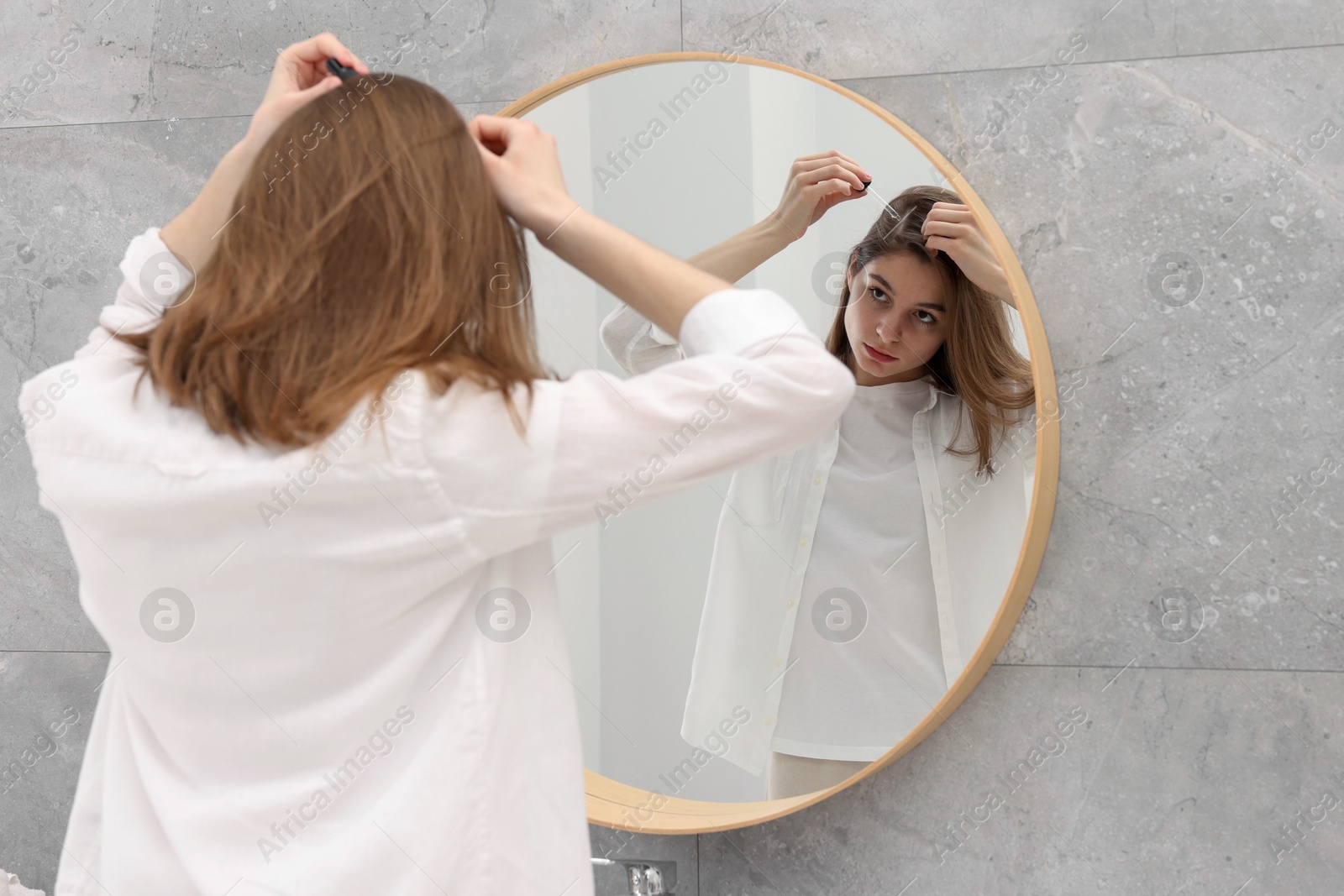 Photo of Hair loss problem. Girl applying serum onto hairline near mirror in bathroom, space for text