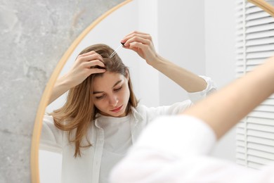 Photo of Hair loss problem. Girl applying serum onto hairline near mirror in bathroom