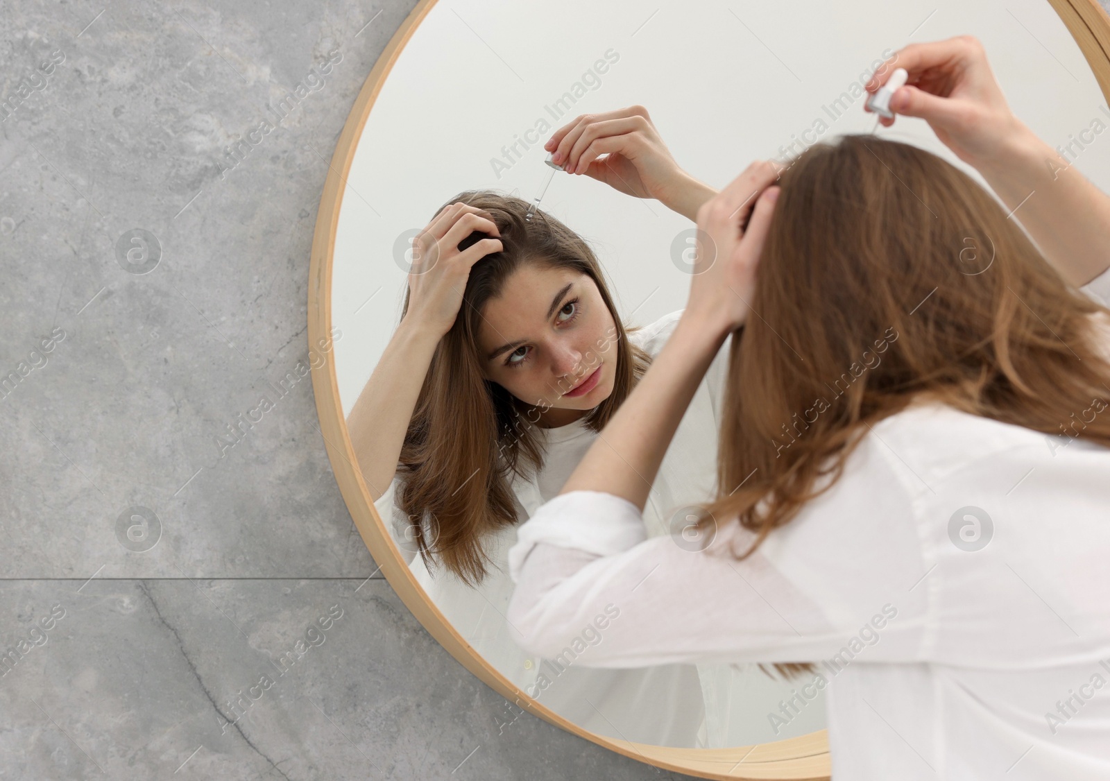 Photo of Hair loss problem. Girl applying serum onto hairline near mirror in bathroom, space for text