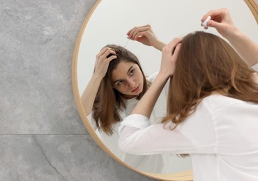 Hair loss problem. Girl applying serum onto hairline near mirror in bathroom, space for text