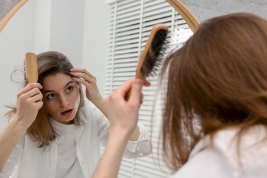 Photo of Girl with hair loss problem near mirror in bathroom