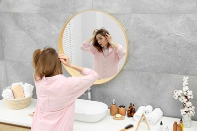 Photo of Girl with hair loss problem near mirror in bathroom