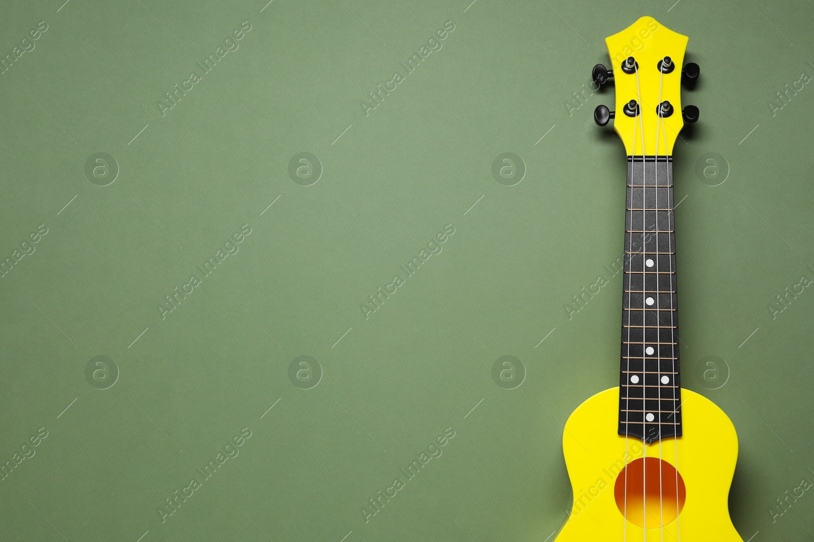 Photo of One ukulele on olive background, top view. Space for text