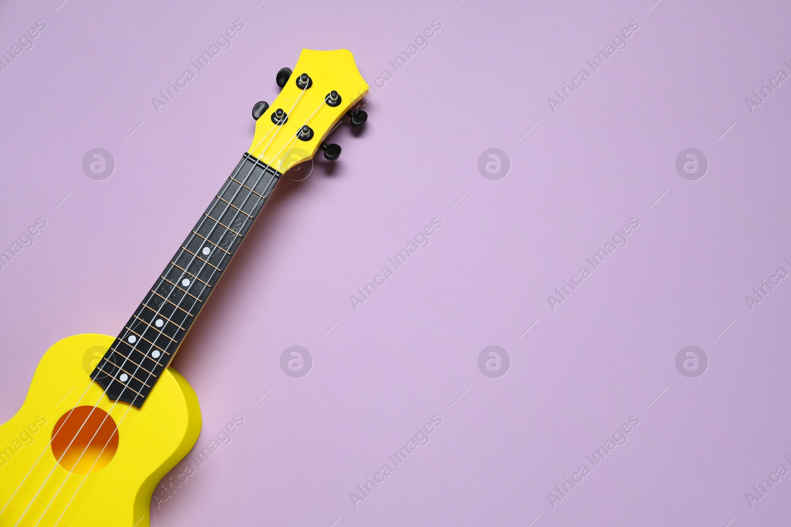 Photo of One ukulele on violet background, top view. Space for text