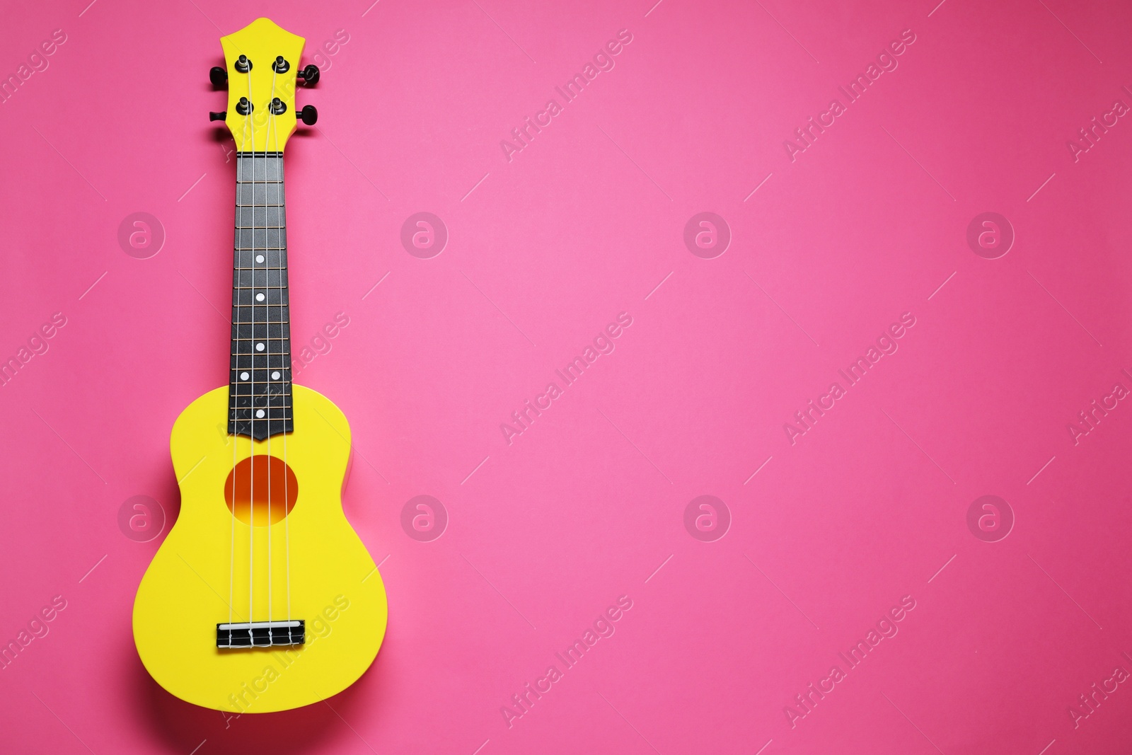 Photo of One ukulele on pink background, top view. Space for text