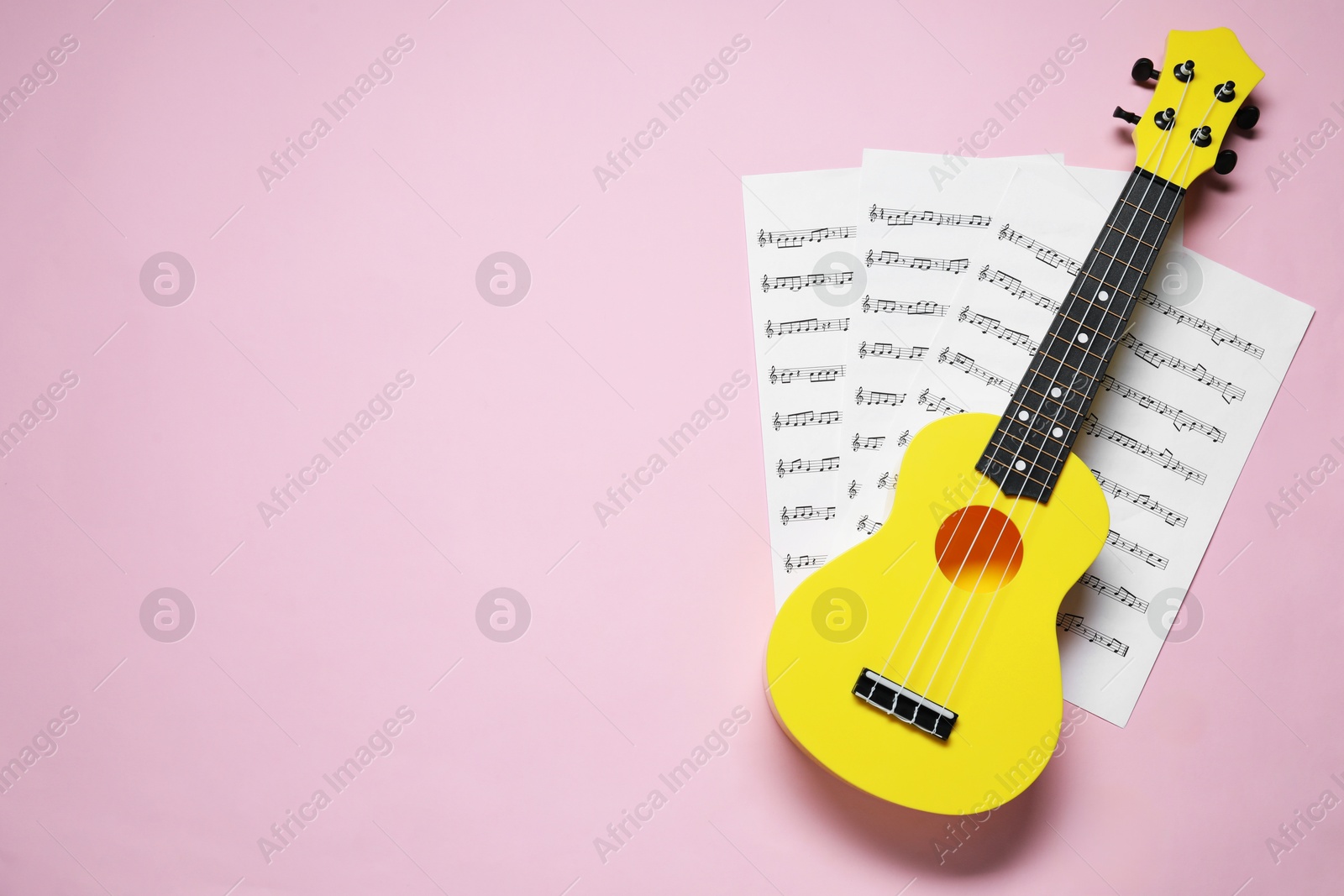 Photo of Ukulele and music sheets on pink background, top view. Space for text