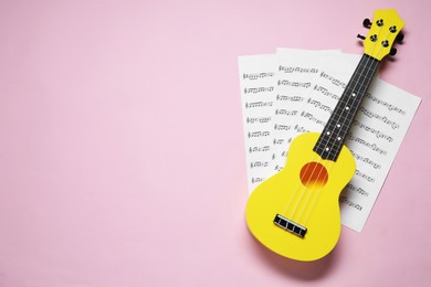 Ukulele and music sheets on pink background, top view. Space for text