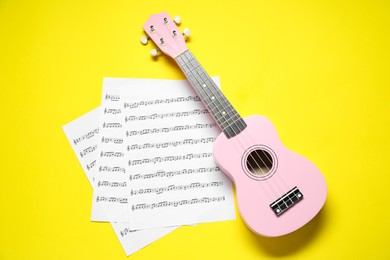 Photo of Ukulele and music sheets on yellow background, top view