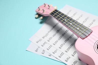 Photo of Ukulele and music sheets on light blue background, space for text