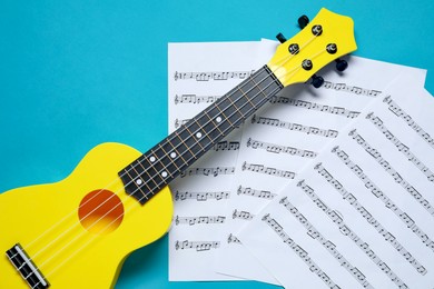 Photo of Ukulele and music sheets on light blue background, flat lay