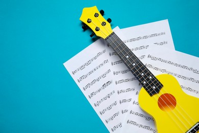 Photo of Ukulele and music sheets on light blue background, top view. Space for text