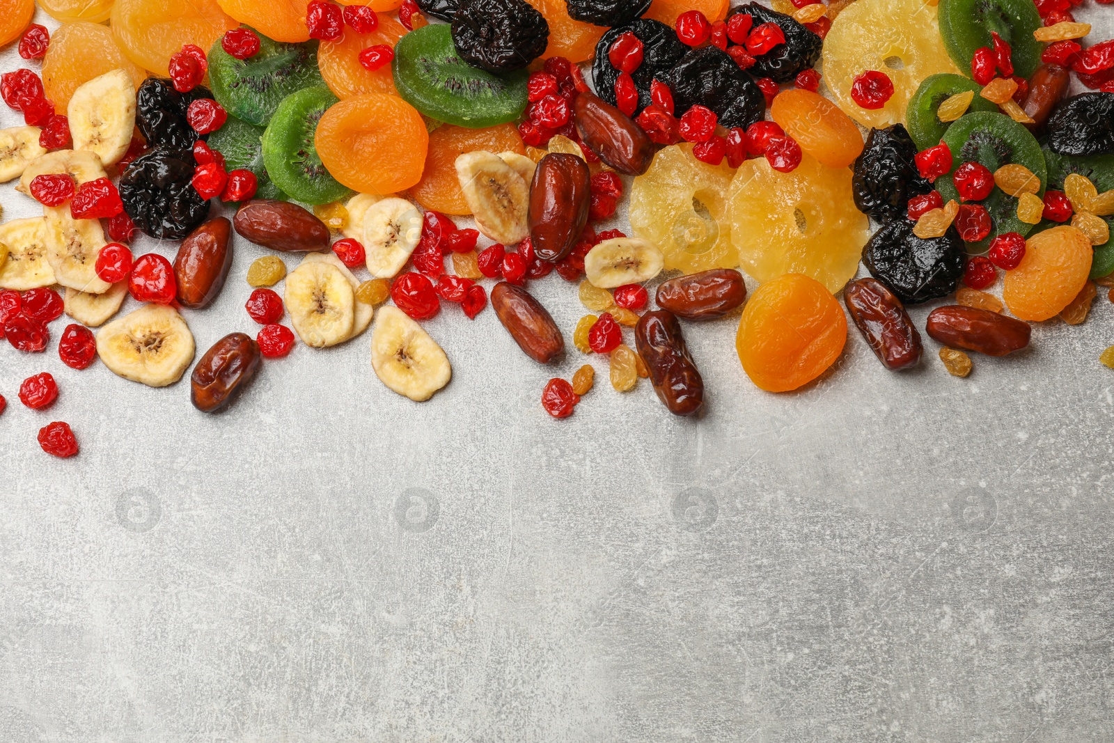 Photo of Mix of different dried fruits on gray textured table, top view. Space for text