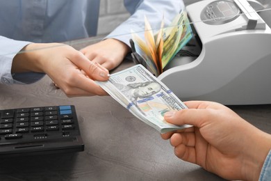 Photo of Cashier giving dollar banknotes to client at table in money exchange, closeup