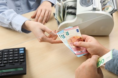 Photo of Client giving euro banknotes to cashier at table in money exchange, closeup