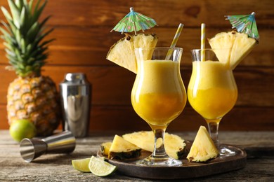 Photo of Tasty pineapple cocktail in glasses served on wooden table