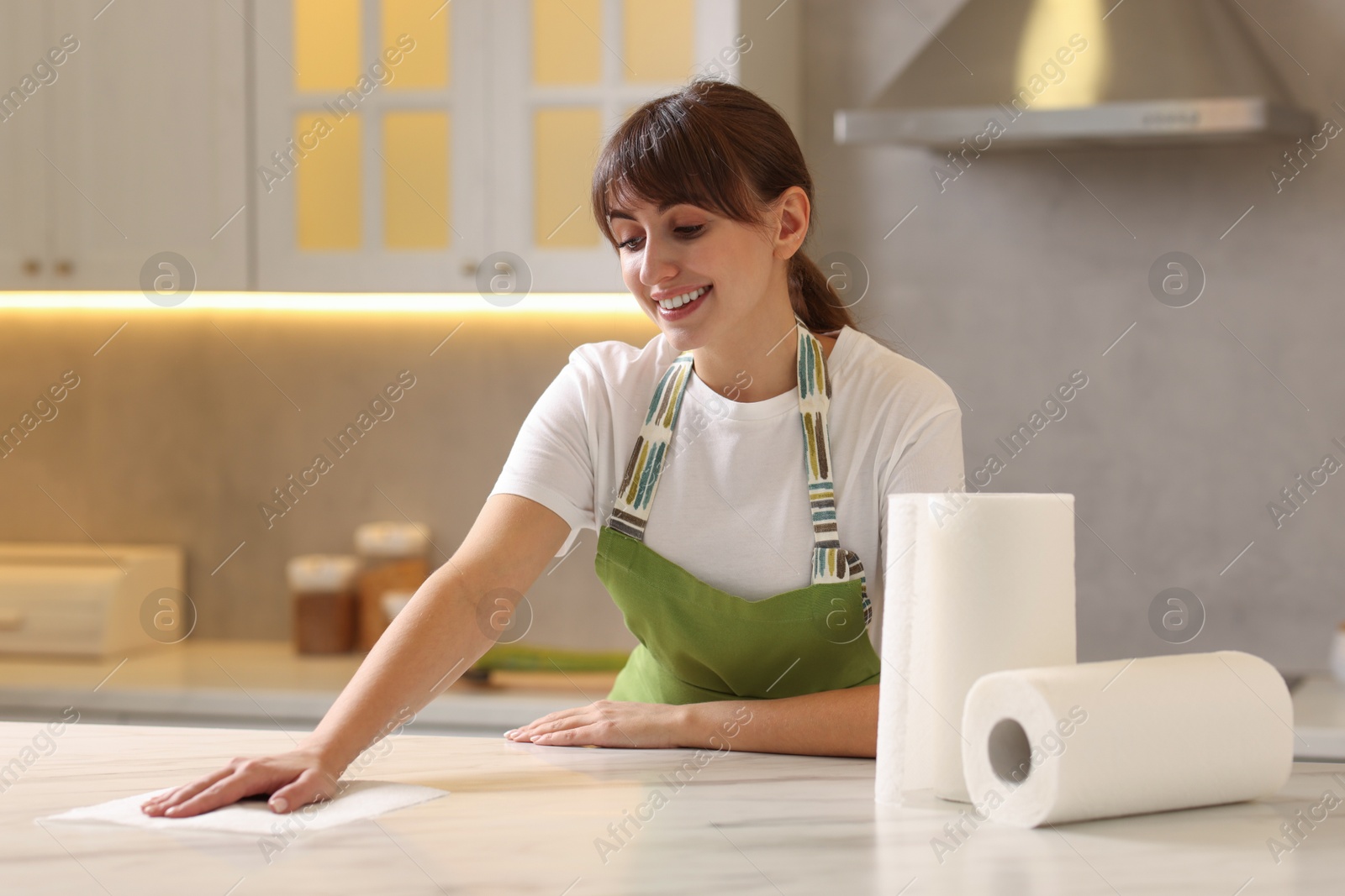 Photo of Woman cleaning white marble table with paper towel in kitchen