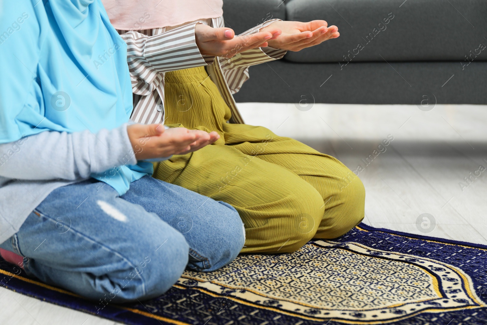 Photo of Muslim woman and her daughter praying on mat at home, closeup