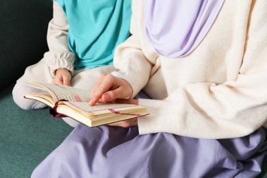 Photo of Muslim woman and her daughter reading Quran at home, closeup