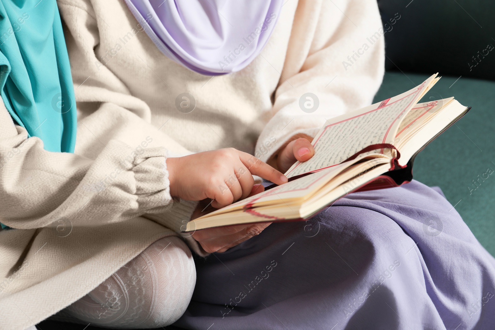 Photo of Muslim woman and her daughter reading Quran at home, closeup