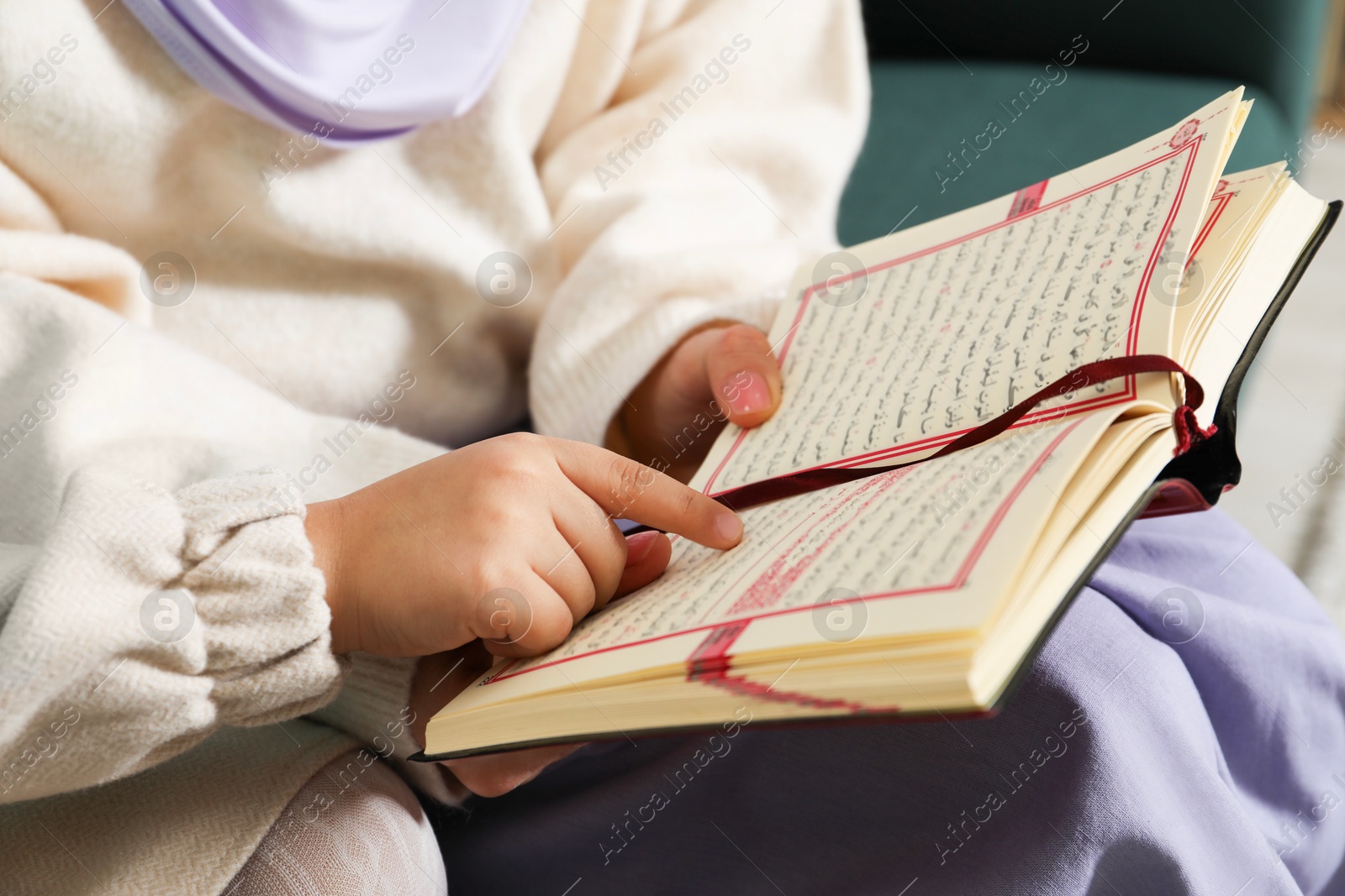 Photo of Muslim woman and her daughter reading Quran at home, closeup