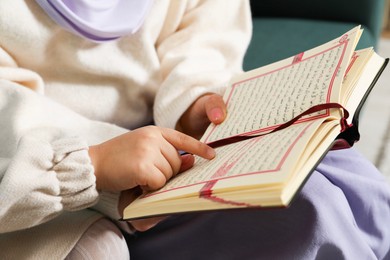 Photo of Muslim woman and her daughter reading Quran at home, closeup