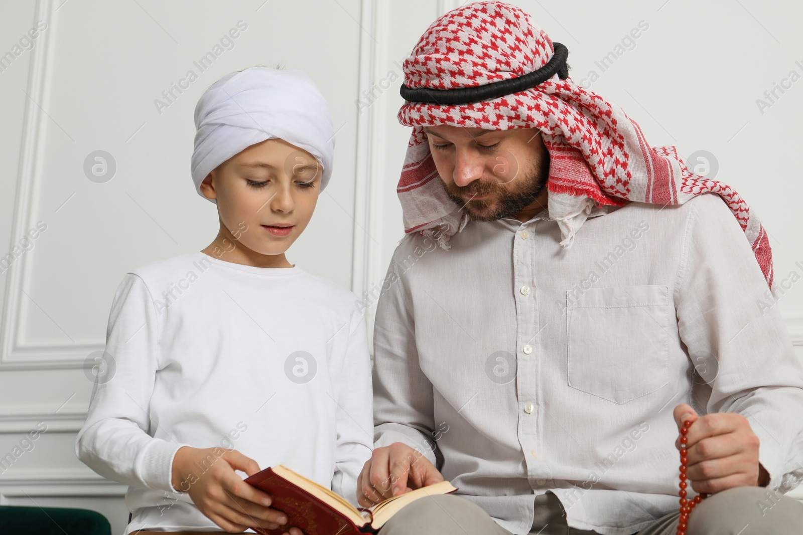 Photo of Muslim man and his son reading Quran at home