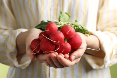 Photo of Woman with bunch of fresh radishes on green background, closeup