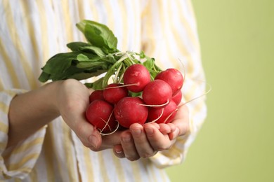 Photo of Woman with bunch of fresh radishes on green background, closeup