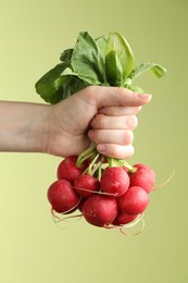 Photo of Woman with bunch of fresh radishes on green background, closeup