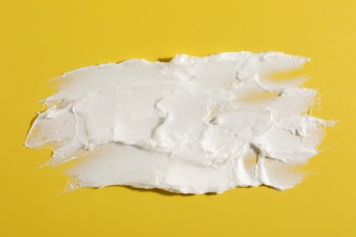 Photo of Cream on dark yellow background, top view. Sample of cosmetic product