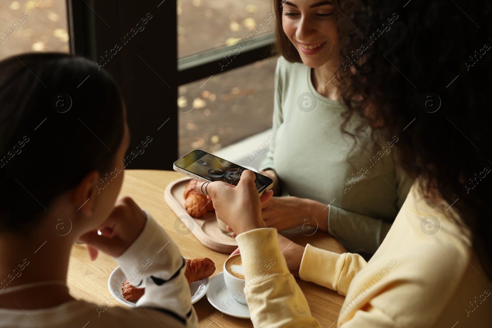 Photo of Woman taking picture of coffee drinks during meeting with her friends in cafe, closeup