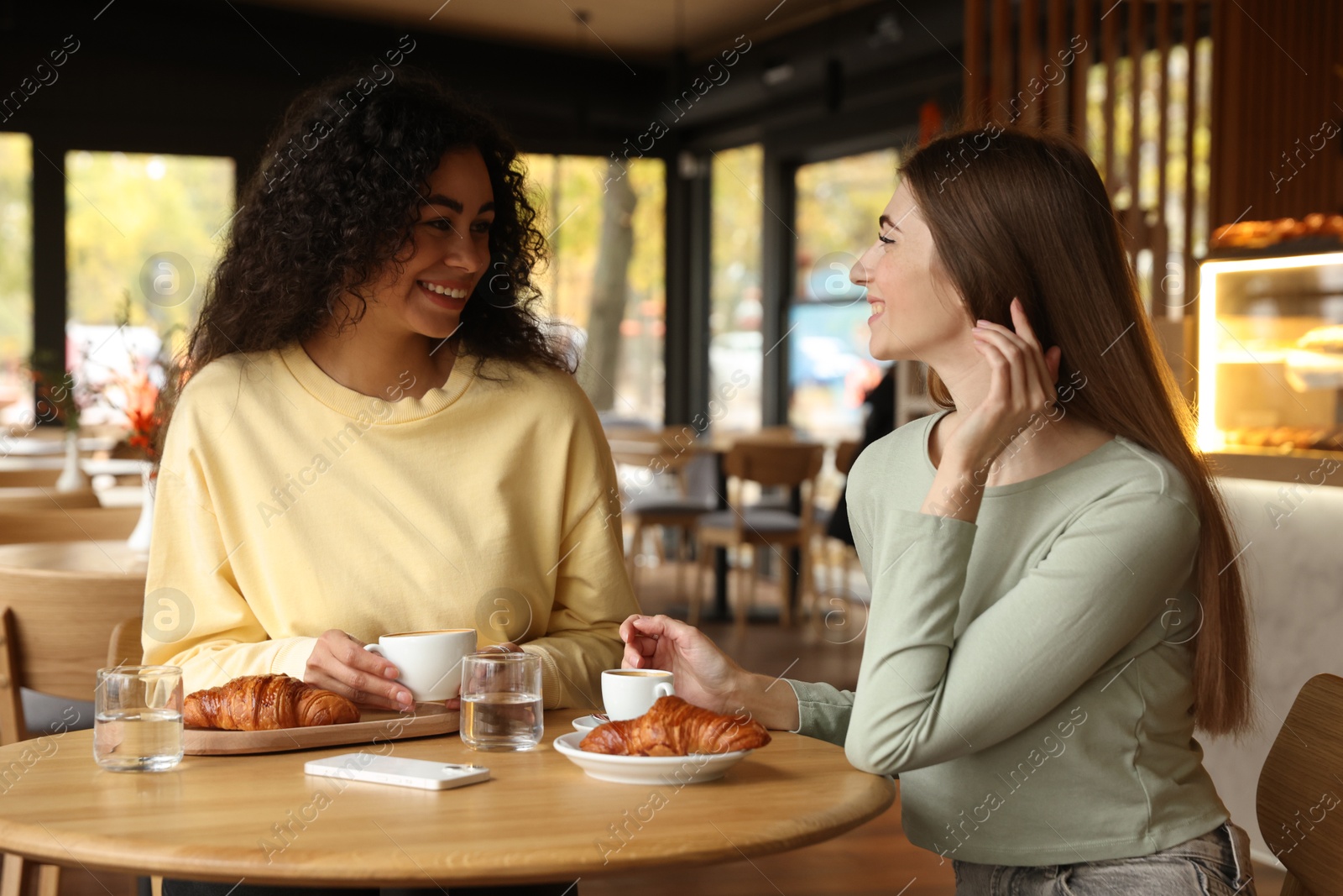 Photo of Happy women with coffee drinks chatting in cafe