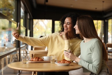 Photo of Happy friends taking selfie during coffee meeting in cafe