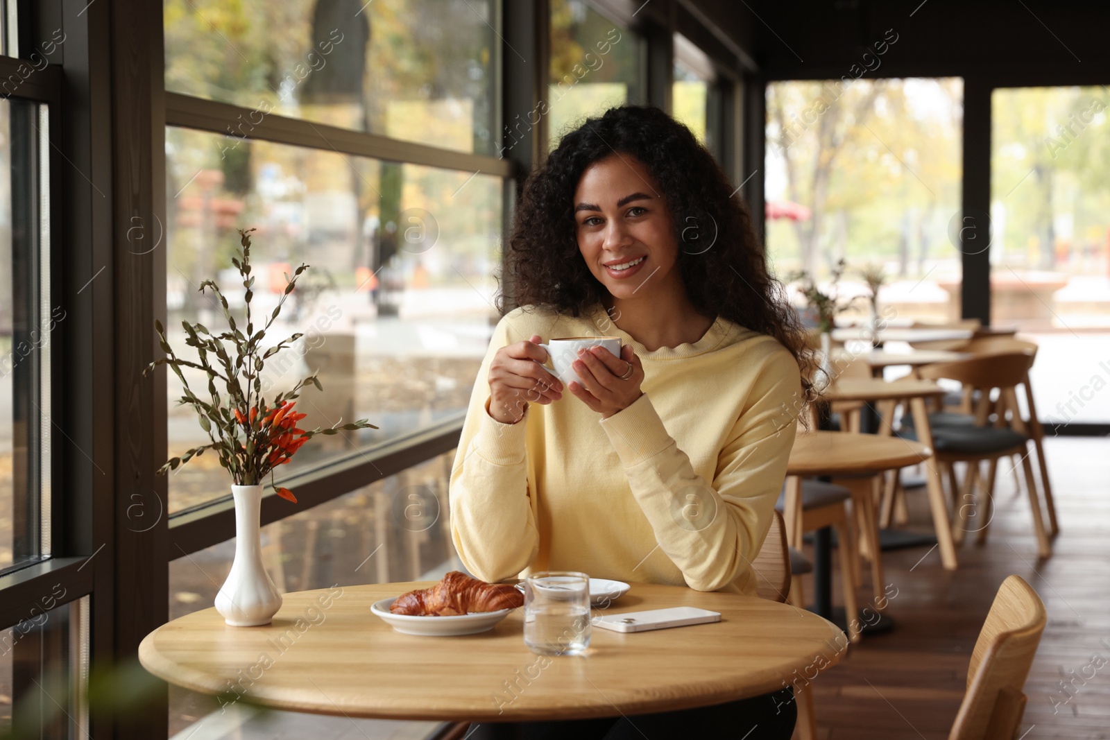 Photo of Woman with coffee and croissant at table in cafe