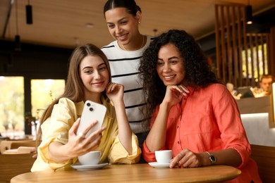 Photo of Happy friends taking selfie during coffee meeting in cafe