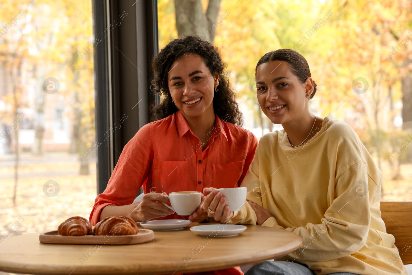 Photo of Happy women with coffee drinks at table in cafe