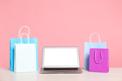 Photo of Internet shopping. Laptop and colorful paper bags on table against pink background