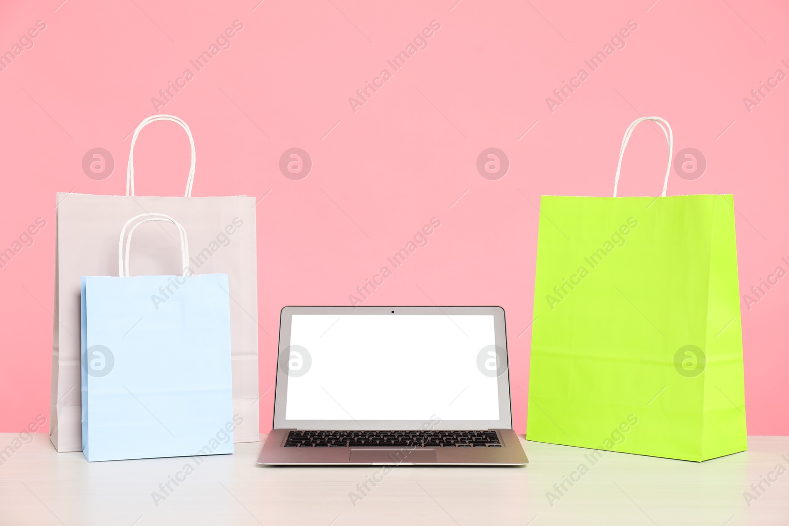 Photo of Internet shopping. Laptop and colorful paper bags on table against pink background