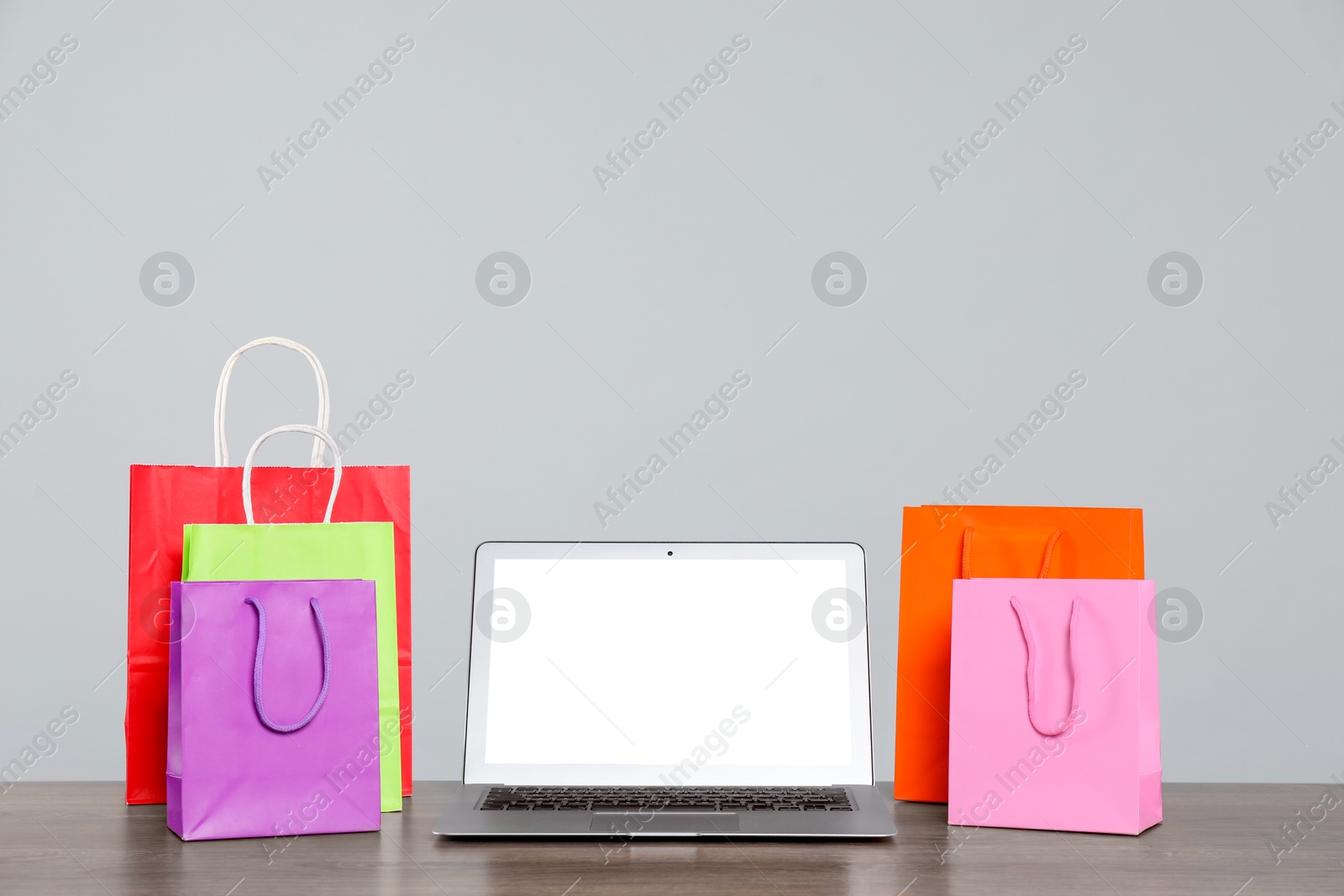 Photo of Internet shopping. Laptop and colorful paper bags on wooden table against grey background