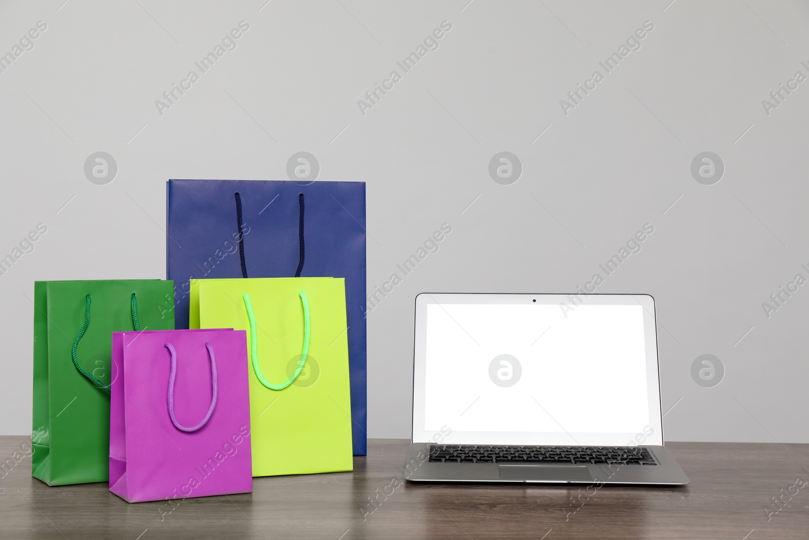 Photo of Internet shopping. Laptop and colorful paper bags on wooden table against grey background