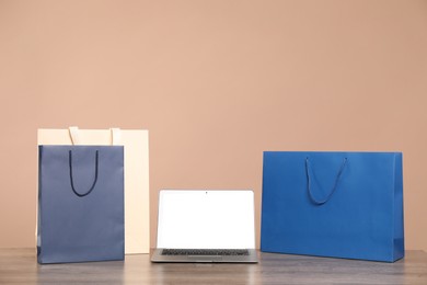 Photo of Internet shopping. Laptop and colorful paper bags on wooden table against brown background