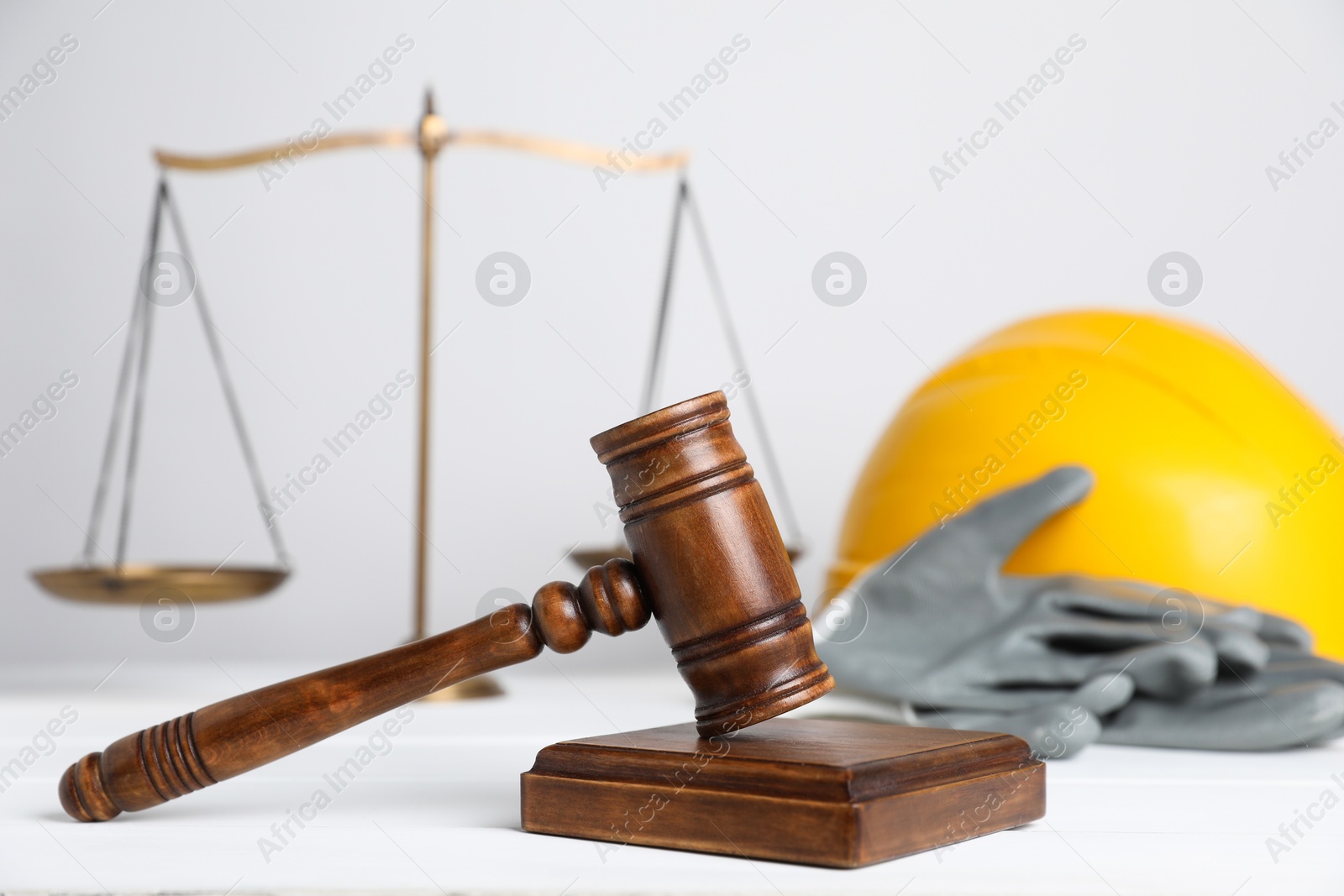 Photo of Accident at work concept. Gavel, scales and construction worker's protective gear on white wooden table, selective focus